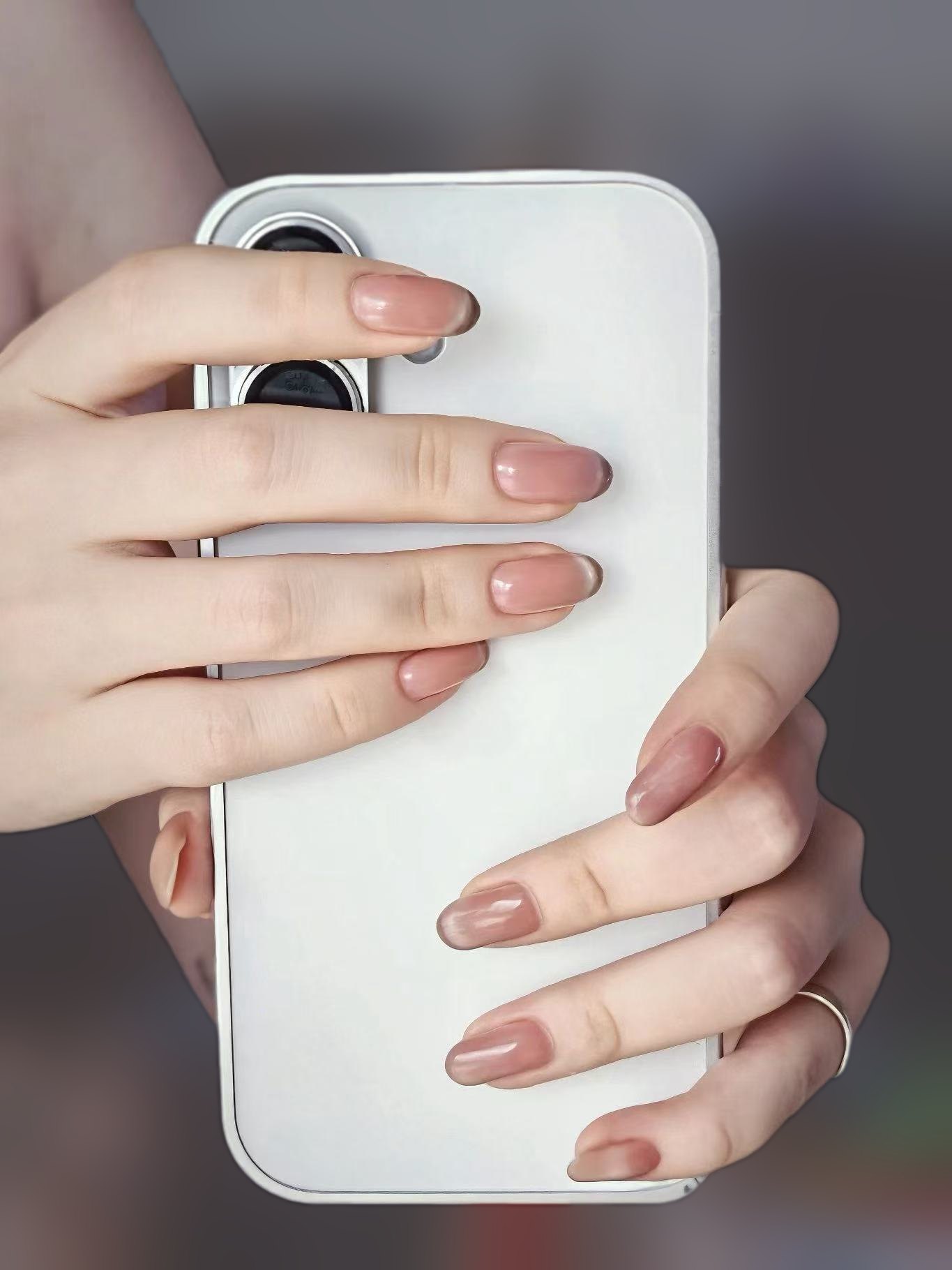 Sheer pink almond nails on two hands holding a white phone